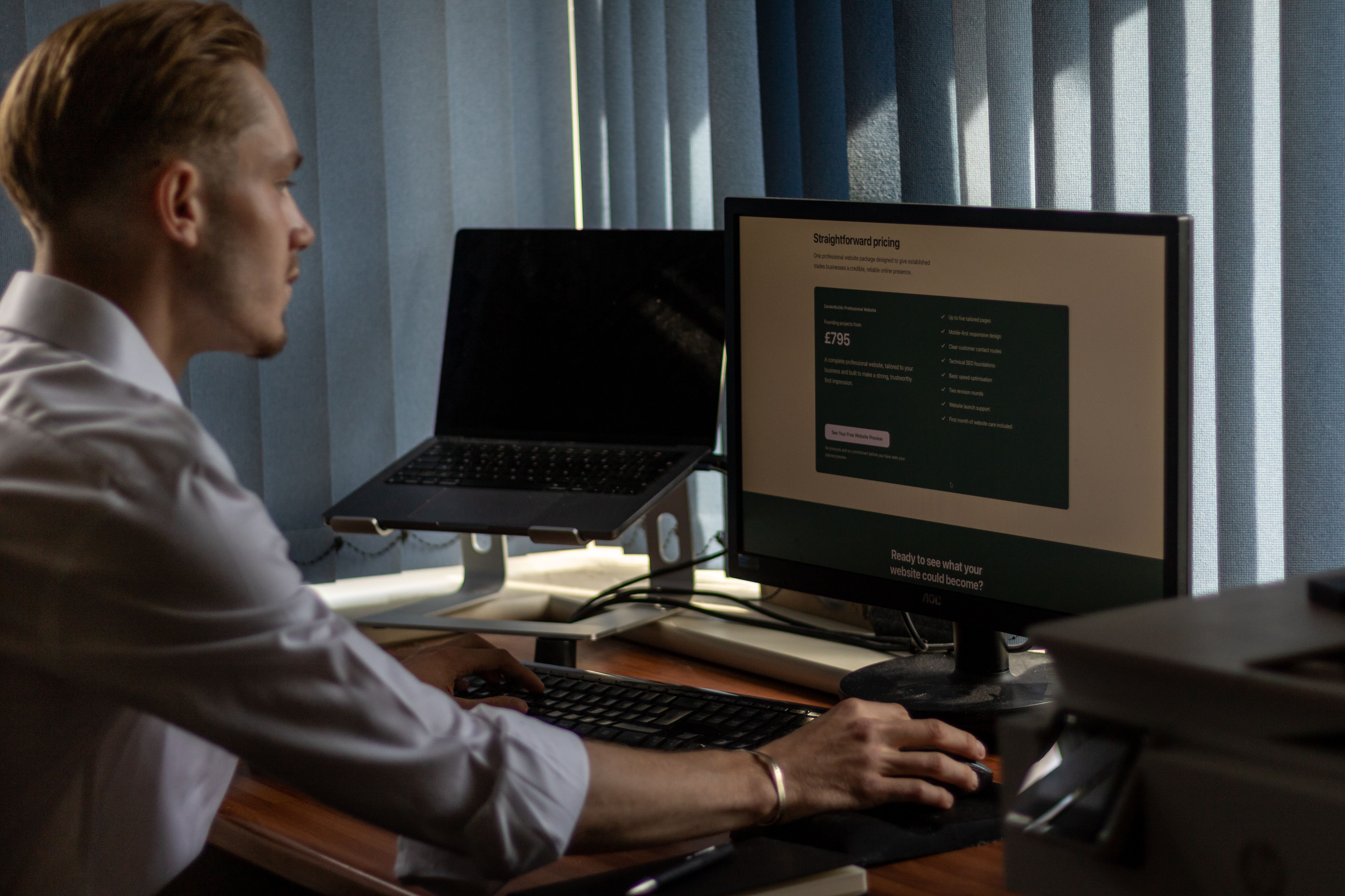 Alex, founder of BuiltByAL, working at his desk with the BuiltByAL website pricing shown on his monitor.
