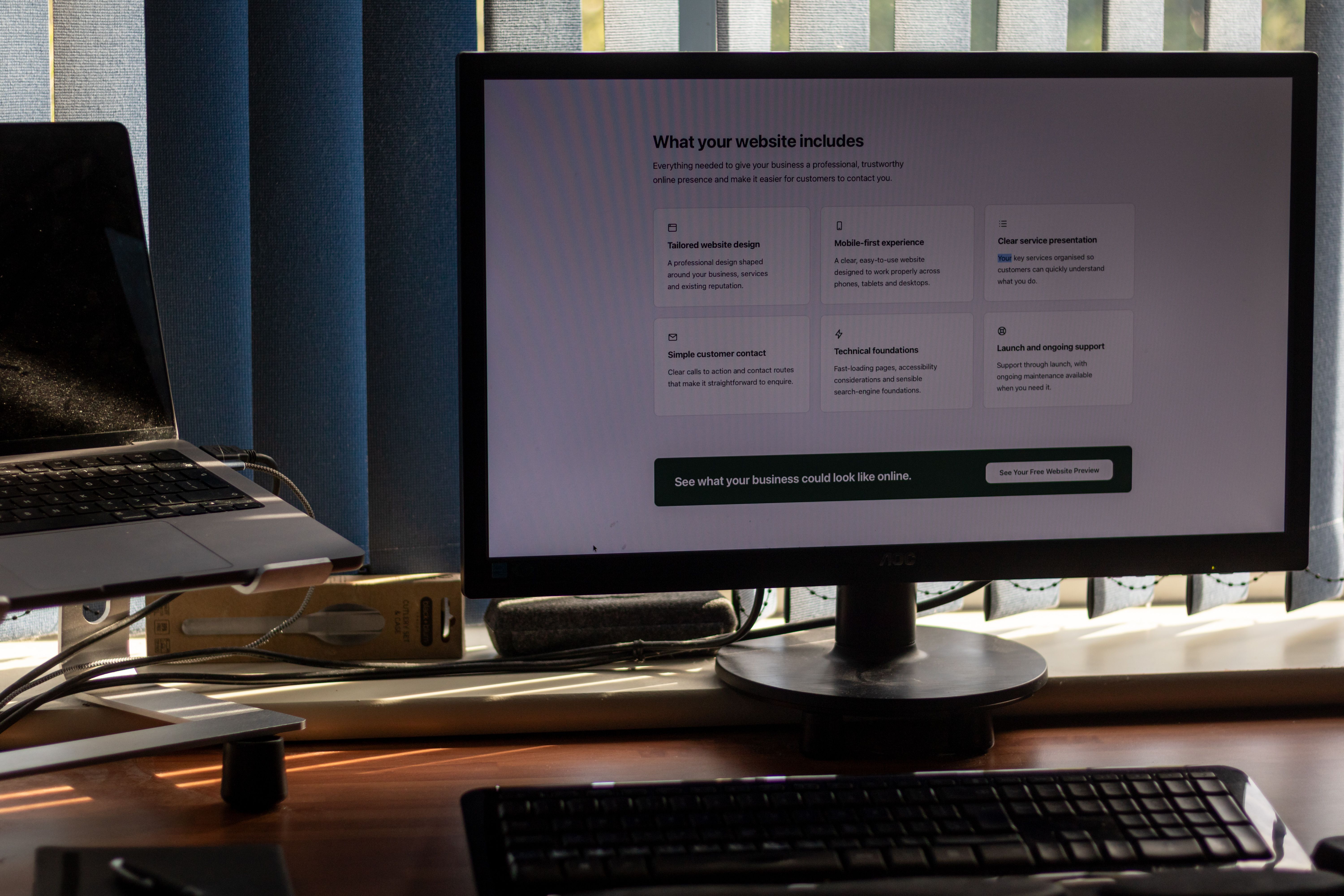 A monitor showing the BuiltByAL website's ‘What your website includes’ section on a tidy desk.