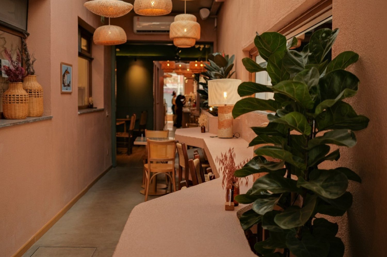 The warm, plant-filled interior of a café with soft lighting and cane chairs