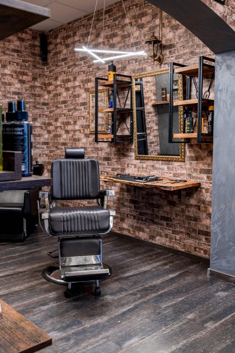 A dark, warmly lit barbershop interior with a leather chair and a gold-framed mirror